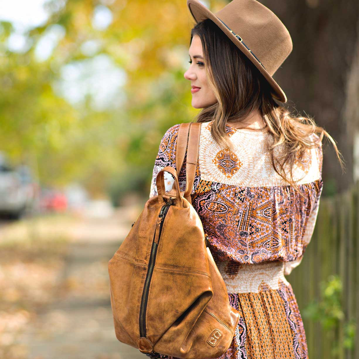 A woman wearing a Delta dress and a Bed Stu hat walking down a sidewalk.