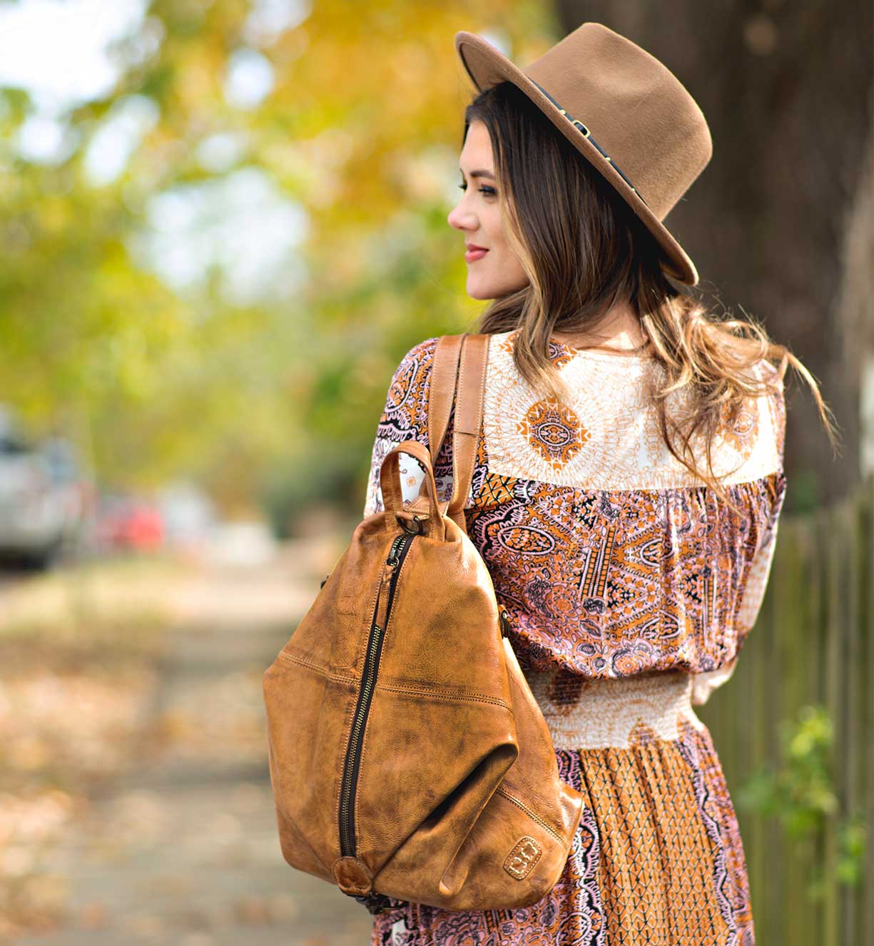 A woman wearing a Delta dress and a Bed Stu hat walking down a sidewalk.