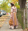 A woman wearing a Delta long dress and Bed Stu hat walking down a sidewalk.