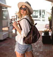 A blonde woman wearing a hat and shorts and carrying a Bed Stu Delta bag.