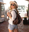 A blonde woman wearing a hat and shorts and carrying a Bed Stu Delta bag.