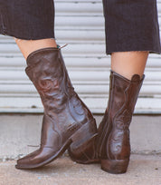 A woman sporting a pair of Bed Stu Deuce western-style cowboy leather boots.