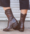 A woman sporting a pair of Bed Stu Deuce western-style cowboy leather boots.