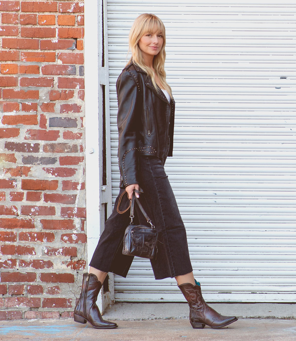 A woman with rustic charm donning a Bed Stu Deuce leather jacket and boots in western style.