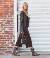 A woman with rustic charm donning a Bed Stu Deuce leather jacket and boots in western style.