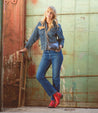 A blonde woman in jeans and a denim jacket, with leather boots, leaning against a Deuce wall by Bed Stu.