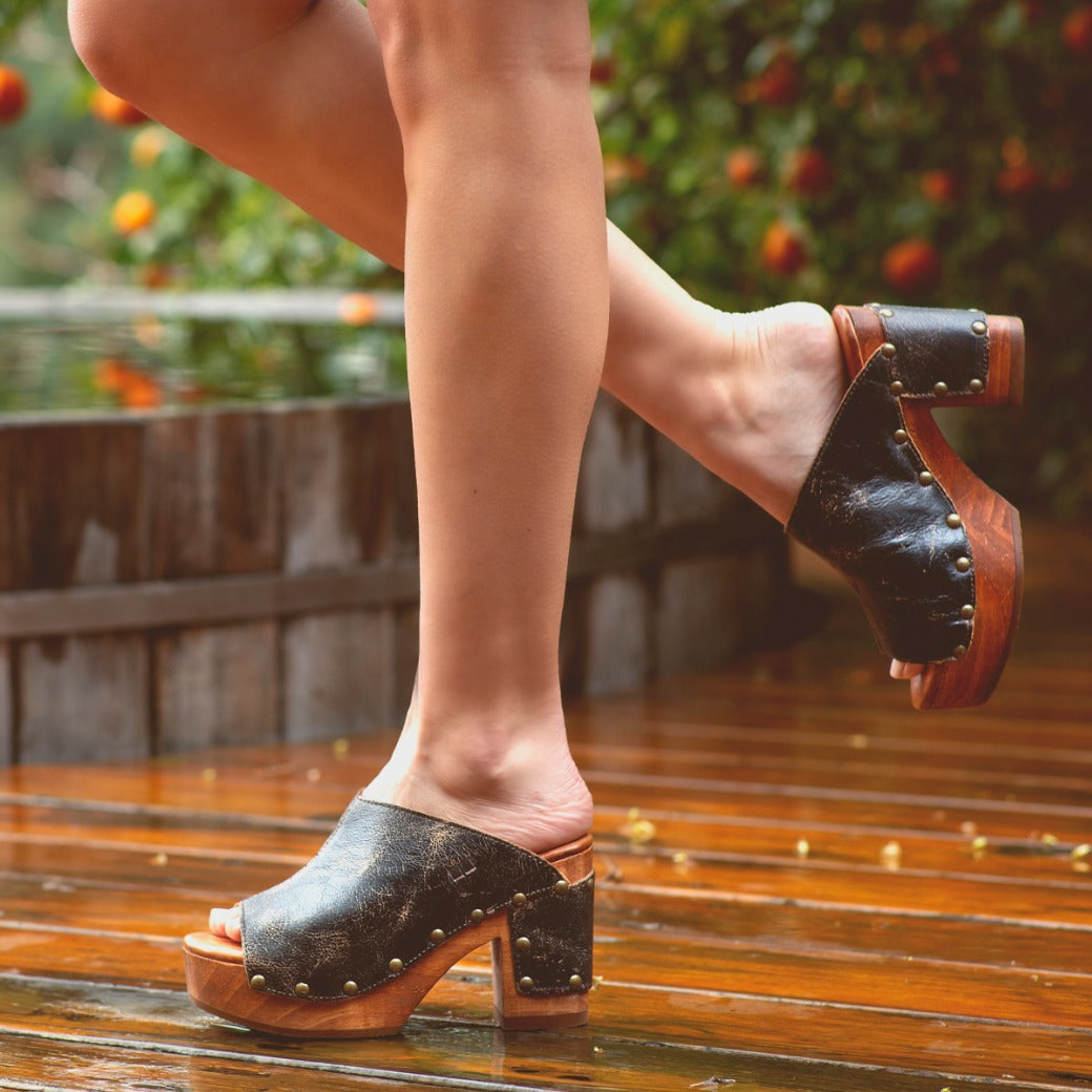 A woman wearing Bed Stu Deva clogs on a wooden deck.