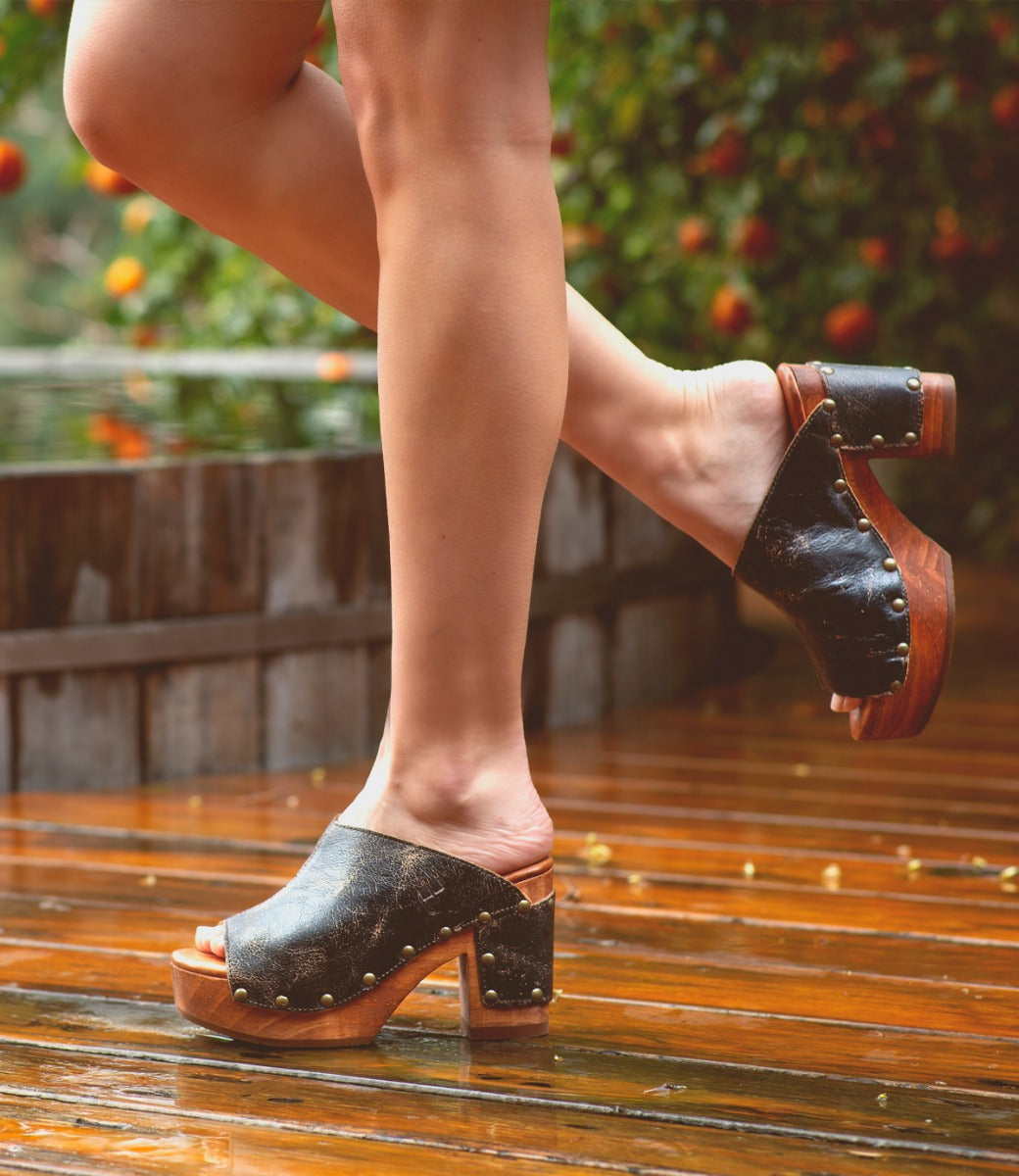 A woman wearing Bed Stu Deva clogs on a wooden deck.