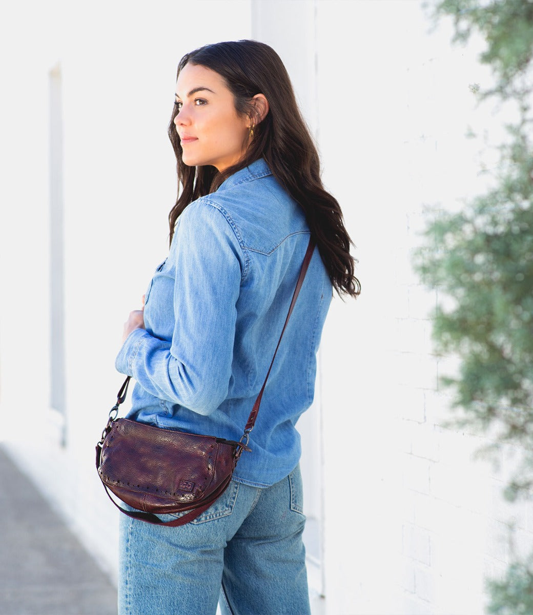 A woman wearing a Dolon by Bed Stu burgundy leather purse.
