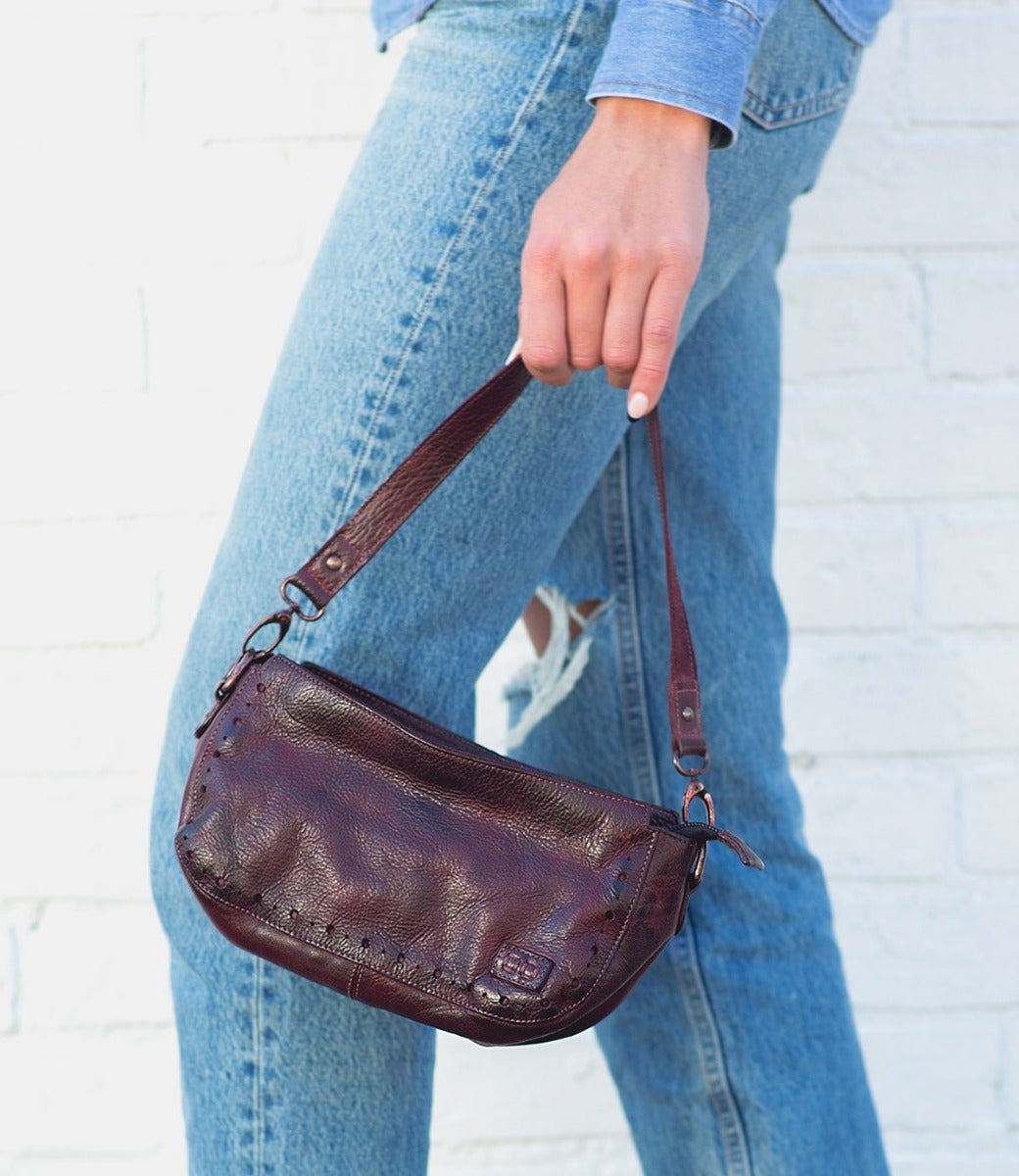 A woman holding a Dolon by Bed Stu burgundy leather purse.