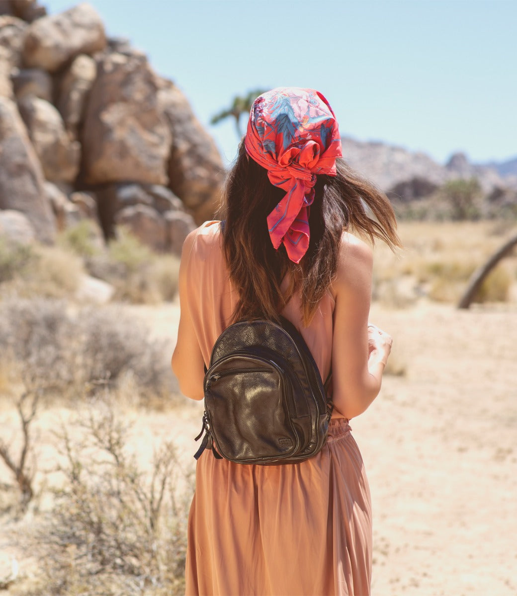 A woman wearing a scarf and a Dominique backpack by Bed Stu in the desert.