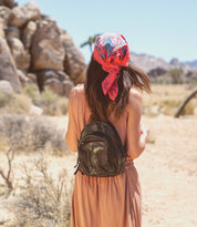 A woman wearing a scarf and a Dominique backpack by Bed Stu in the desert.