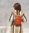 A woman wearing a striped dress and a brown leather Bed Stu Dominique backpack.