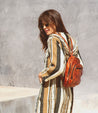 A woman wearing a striped dress and a brown leather Dominique backpack by Bed Stu.