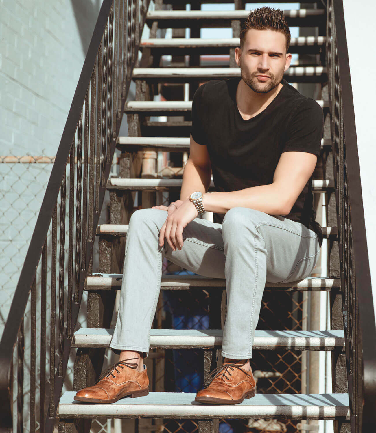 A man sitting on stairs in a black shirt and Bed Stu Donatello shoes.