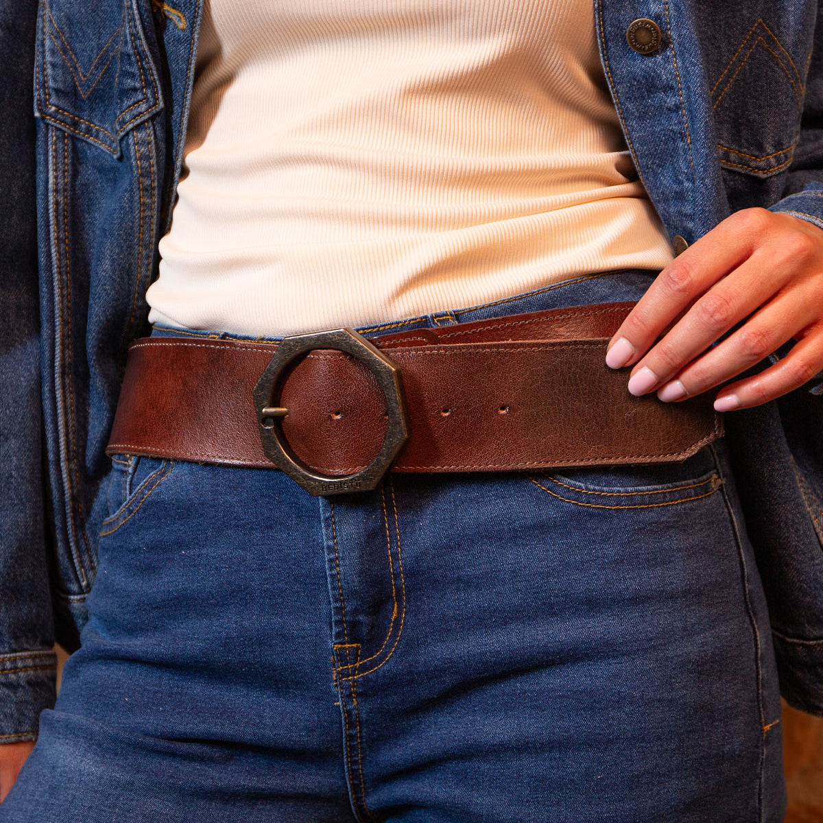 Wearing Bed Stu’s Dreampath belt, a wide genuine leather accessory with a large octagon buckle, paired with a cream ribbed shirt, blue denim jacket, and jeans for rugged durability and style.