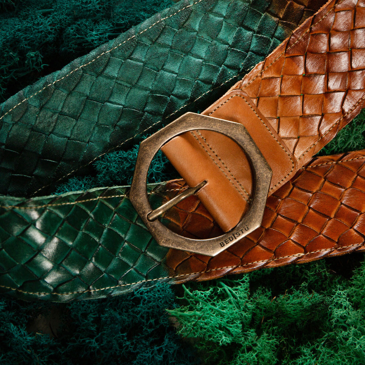 Two Bed Stu Dreamweaver vintage woven leather belts, one green and one brown with hexagonal metal buckles, are displayed on a textured green surface.
