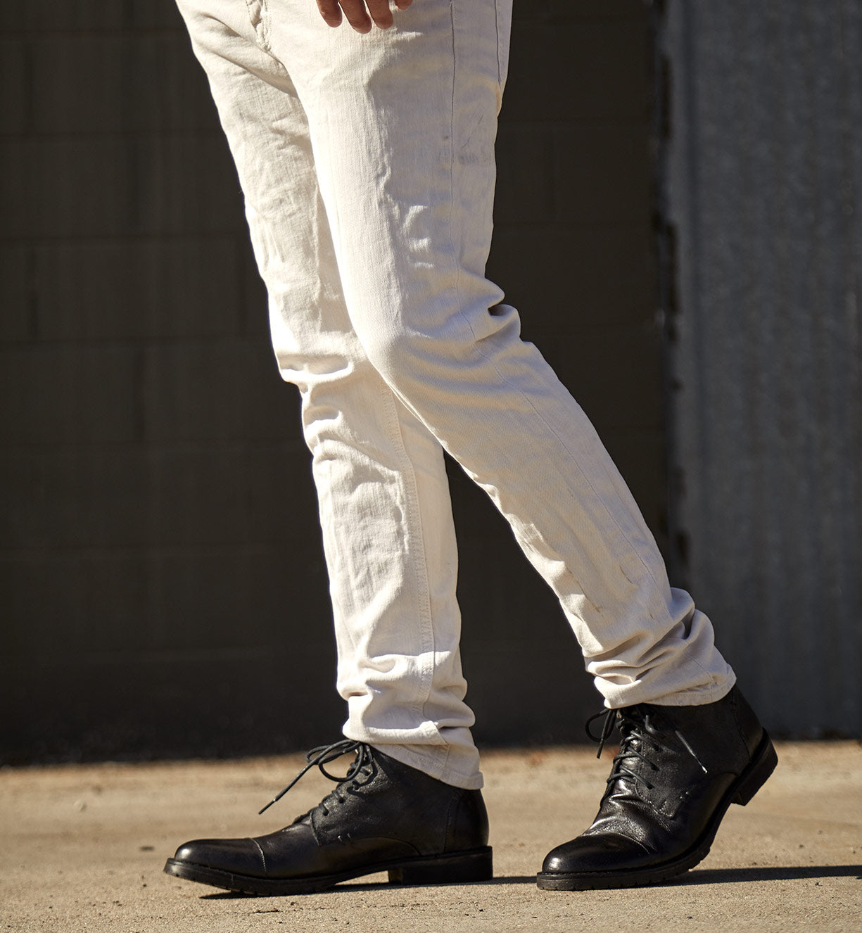 A man wearing white "Dreck" jeans and black "Bed Stu" shoes.