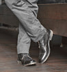 A man wearing a pair of gray Dreck pants and a pair of black Bed Stu shoes.