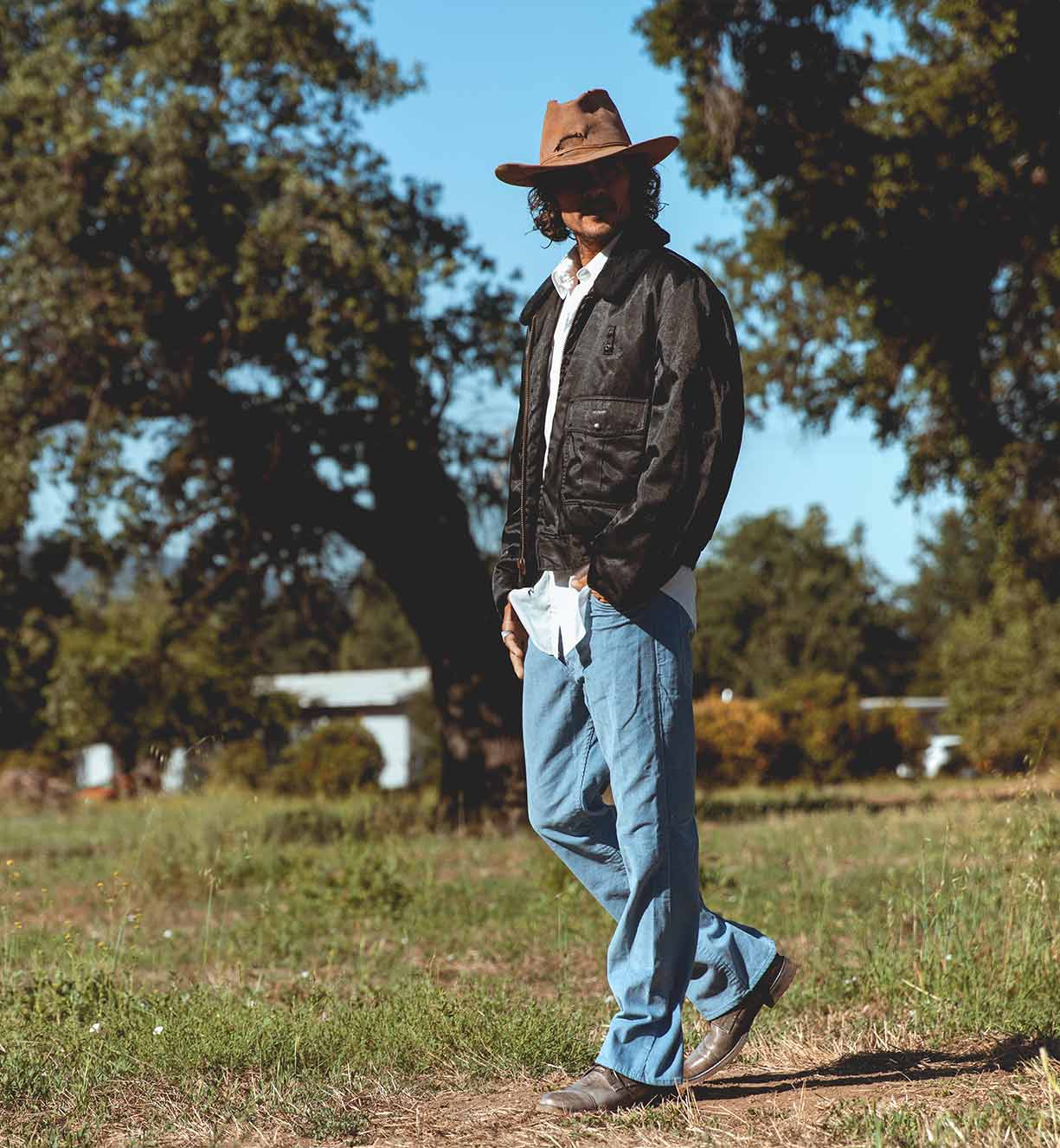 A man wearing a Bed Stu hat and jeans standing in a field.