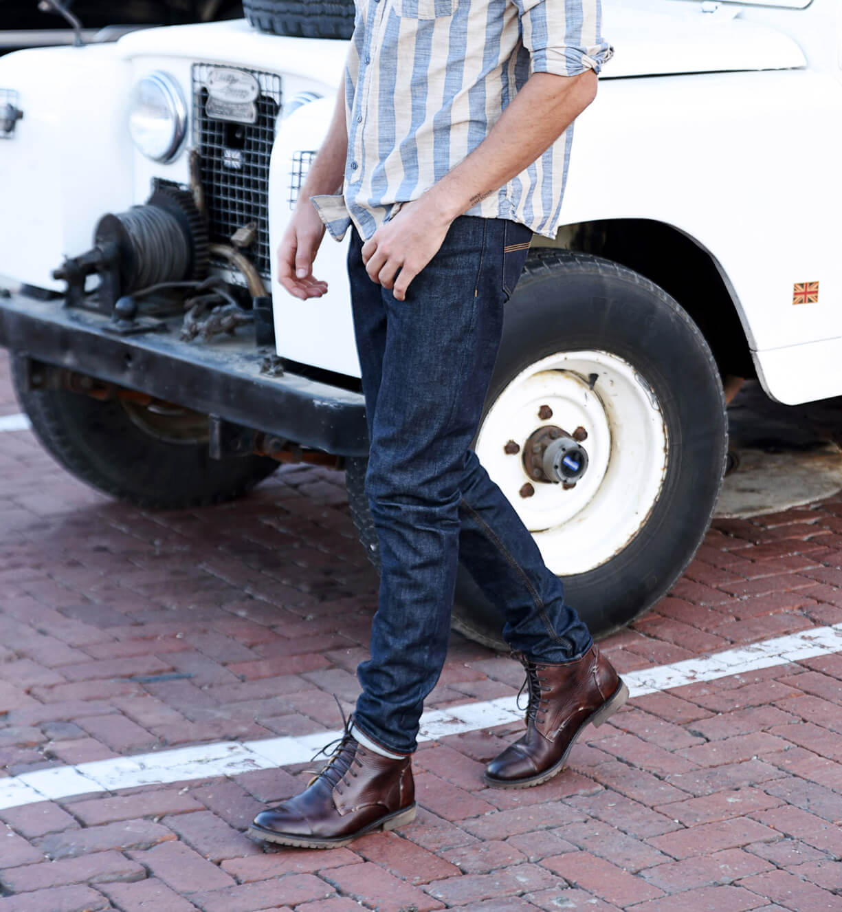 A man wearing a striped shirt and jeans is standing next to a white Bed Stu jeep.
