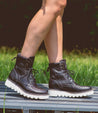 A woman's legs standing on a bench wearing the Bed Stu Elisha II shoes in a grassy area.