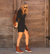 A woman in a blue dress and brown Bed Stu Elisha II boots standing in front of a wooden door.