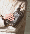 A woman wearing a sweater holding a Bed Stu Encase leather purse.