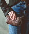 A woman holding a Bed Stu Encase brown leather purse.