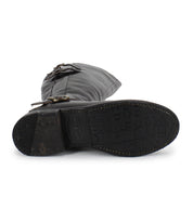 The image shows the bottom view of Bed Stu's Essence, a black hand-finished leather boot with two side buckles and visible tread patterns, reflecting classic equestrian design.