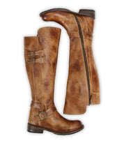 A pair of Bed Stu Essence brown leather knee-high riding boots featuring buckles; one boot stands upright while the other lies on its side, revealing a zipper and hand-finished leather for classic equestrian style.