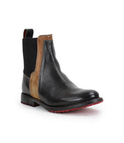 The Bed Stu Ethic is a black vegetable-tanned leather Chelsea boot with a brown accent strip, elastic side panels, back pull tab, and vibrant red Vibram sole, shown on a white background.