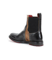 The Bed Stu Ethic is a black vegetable-tanned leather Chelsea boot featuring brown accents, red interior lining, and an elastic side panel, displayed from the rear side angle on a white background.