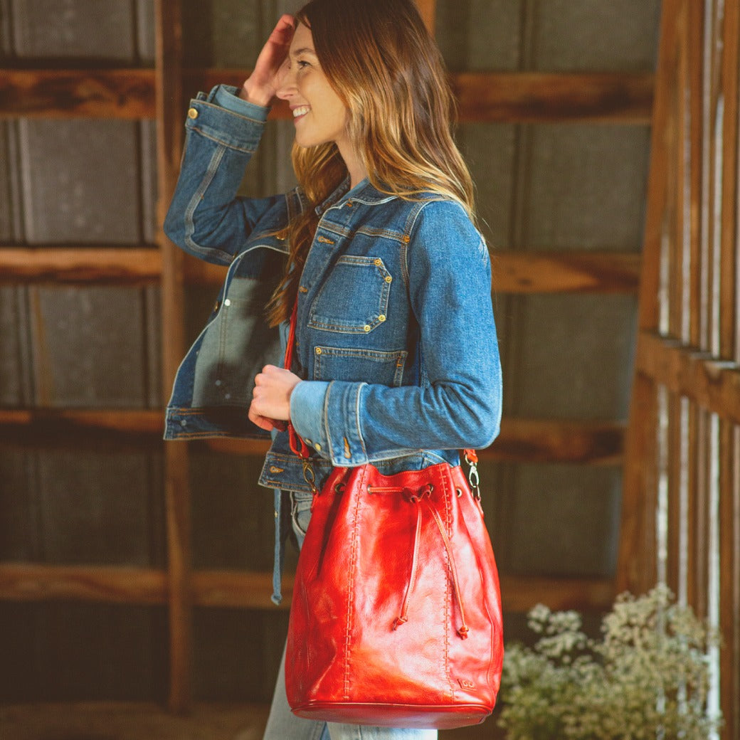 A woman wearing a denim jacket holding a red leather Bed Stu Eve bag.