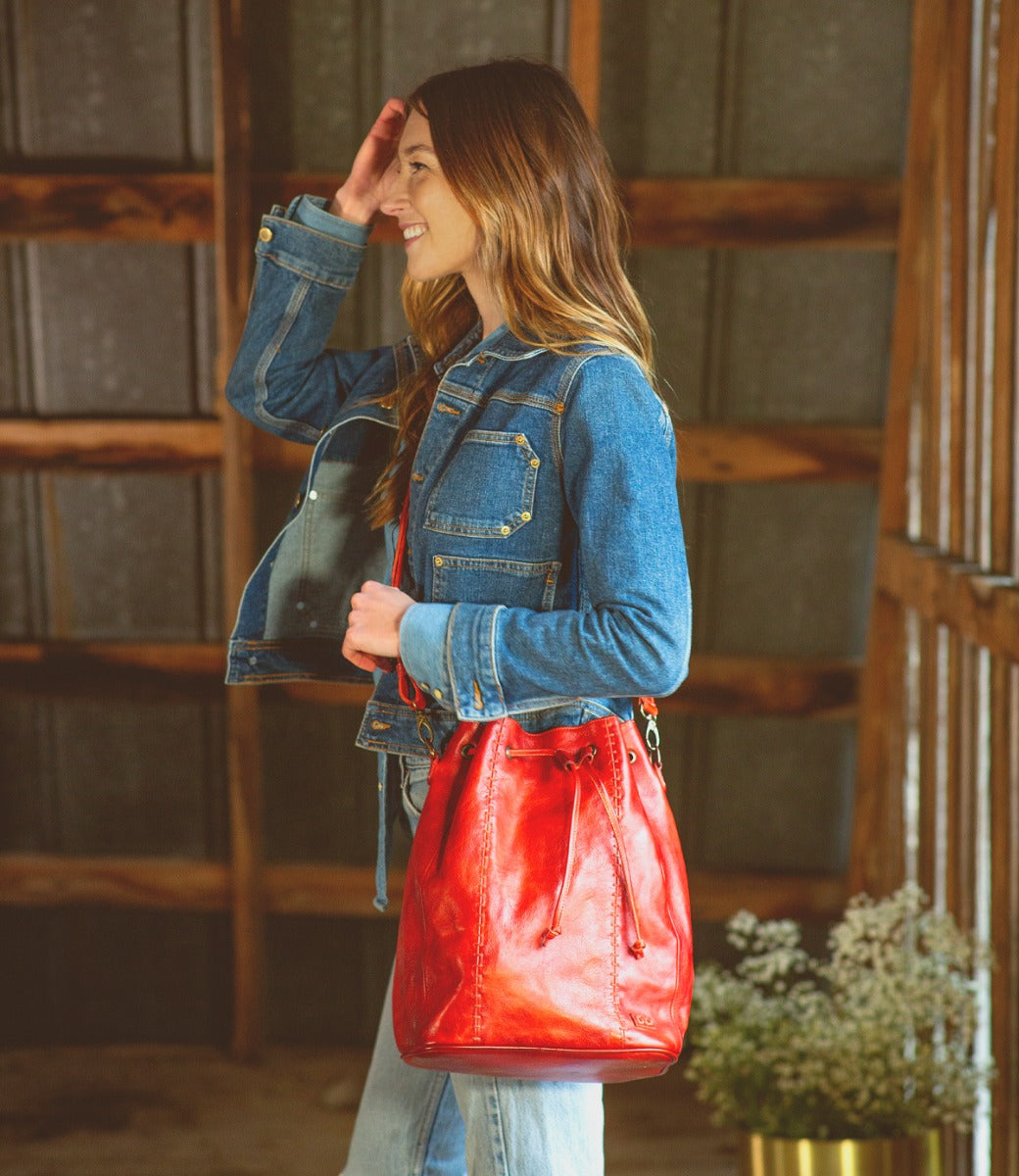 A woman wearing a denim jacket holding a red leather Bed Stu Eve bag.