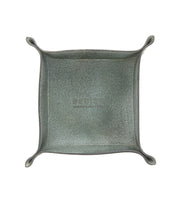 A square, gray-green Expanse Catchall Tray with raised sides and curled corners. Perfect for holding loose change and keys, the surface boasts a textured finish by Bed Stu.