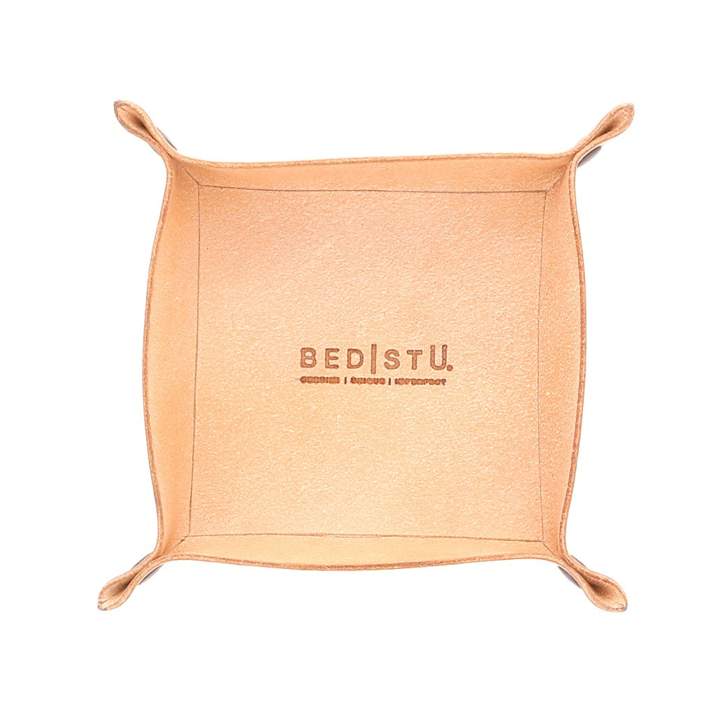 A square, tan leather Expanse Catchall Tray with "Bed Stu" and additional text engraved on the base, perfect for holding keys or loose change, featuring folded corners.