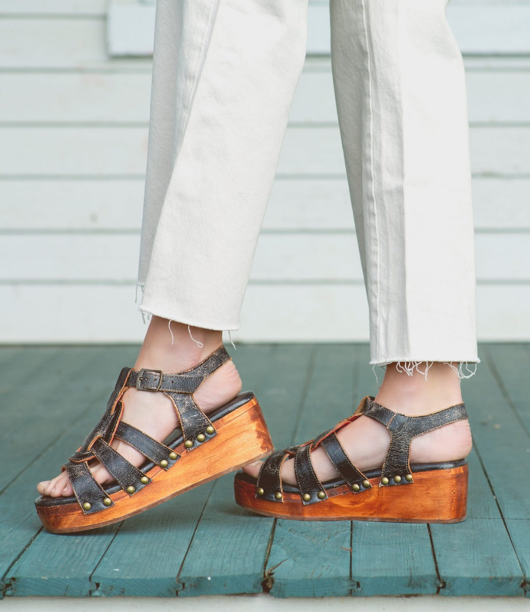 A woman wearing a pair of Bed Stu distressed black Fabiola wooden sandals standing on a porch.