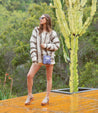 A woman is standing on a wooden deck, wearing Fabiola sandals, in front of a cactus.