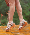 A woman wearing Fabiola sandals on a wooden deck.
