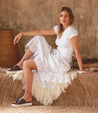 A woman wearing the Bed Stu Fairlee II dress and sandals sitting on a hay bale.
