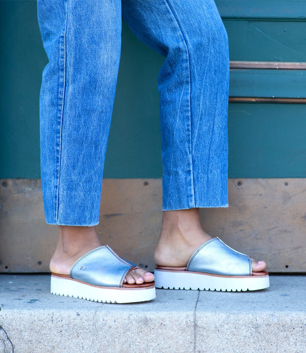 A woman wearing a pair of Bed Stu Fairlee II silver slide sandals.
