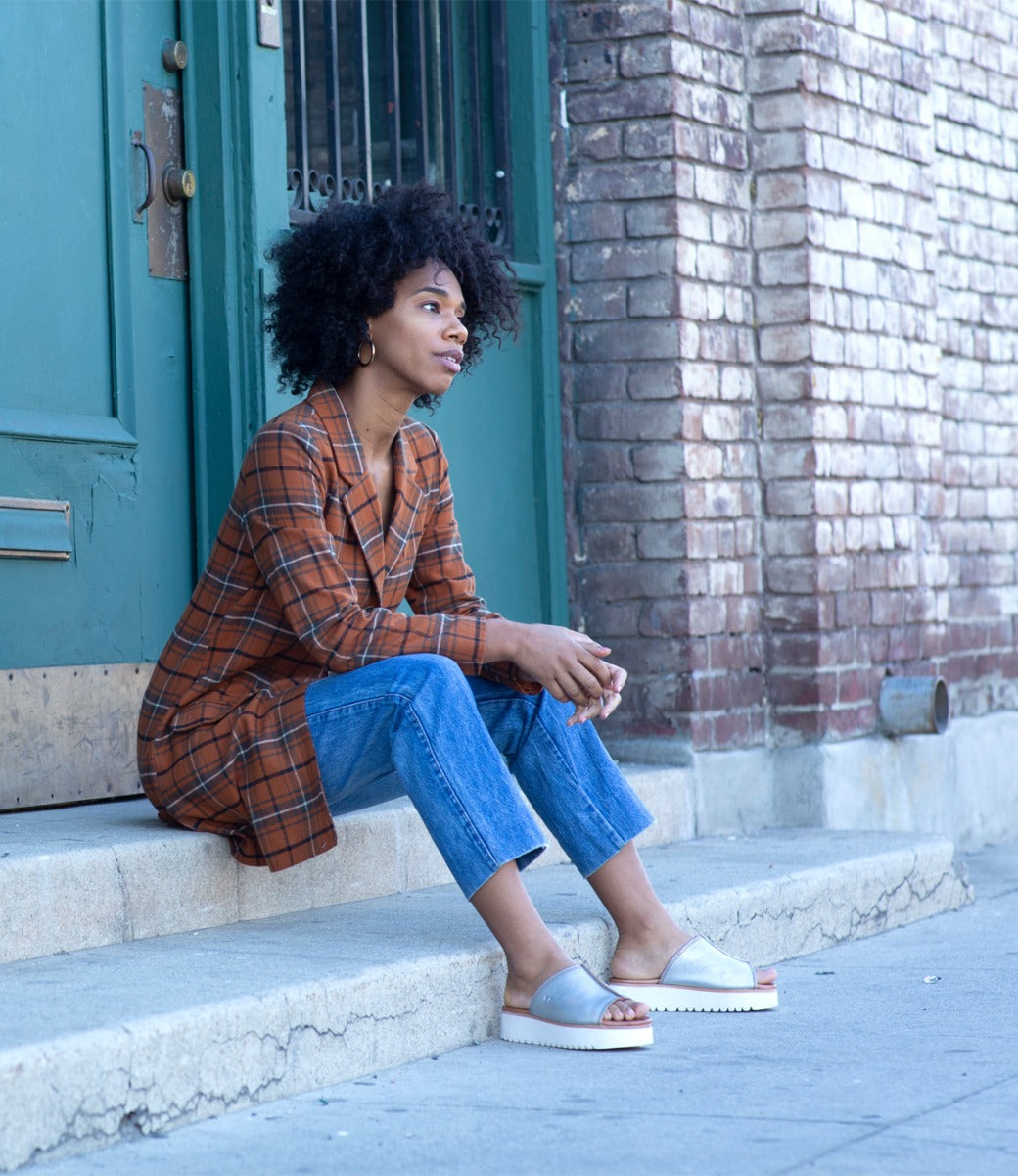 A woman in a plaid shirt sitting on the steps of a building wearing Fairlee II by Bed Stu.