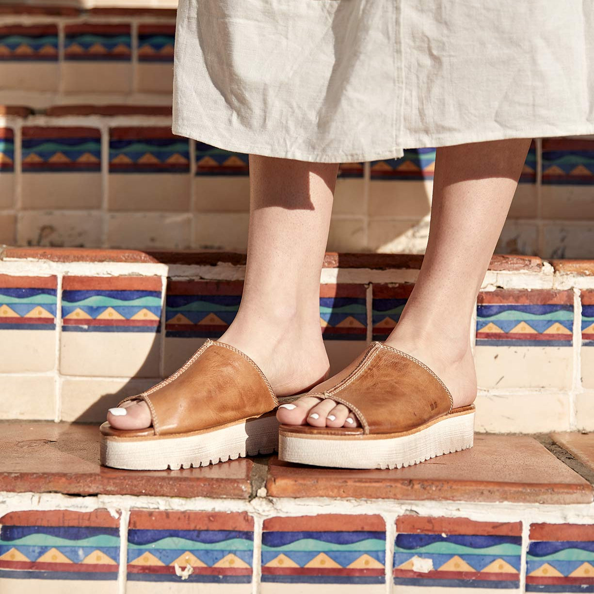 A woman is standing on a set of steps wearing Bed Stu Fairlee II sandals.