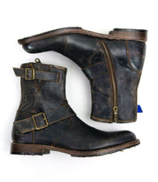 The "Fellow" ankle boots from Bed Stu are crafted from distressed brown leather with a subtle moto-inspired design, featuring side zippers and buckles. These men's leather boots boast Goodyear welt construction for enhanced durability and are elegantly presented from a side and top view on a white background.