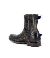 The Fellow boot by Bed Stu, made of brown leather with a moto-inspired design, includes a side zipper and a blue pull tab at the back, showcased from a side view.