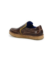 The Freestyle slip-on shoe by Bed Stu is crafted from brown leather, featuring visible detailing, a blue inner lining, and a beige sole. Angled to showcase its back and side views, this shoe exudes casual sophistication.
