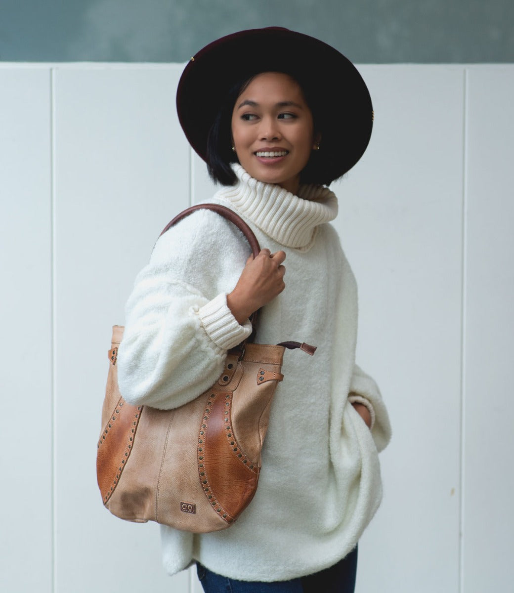A woman in a white sweater and hat holding a Bed Stu Gala bag.
