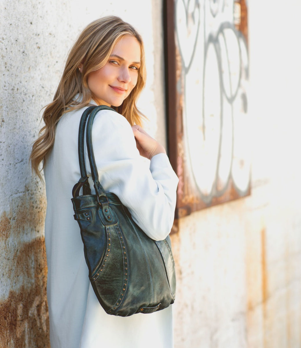 A woman in a white coat holding a Bed Stu Gala green leather bag.