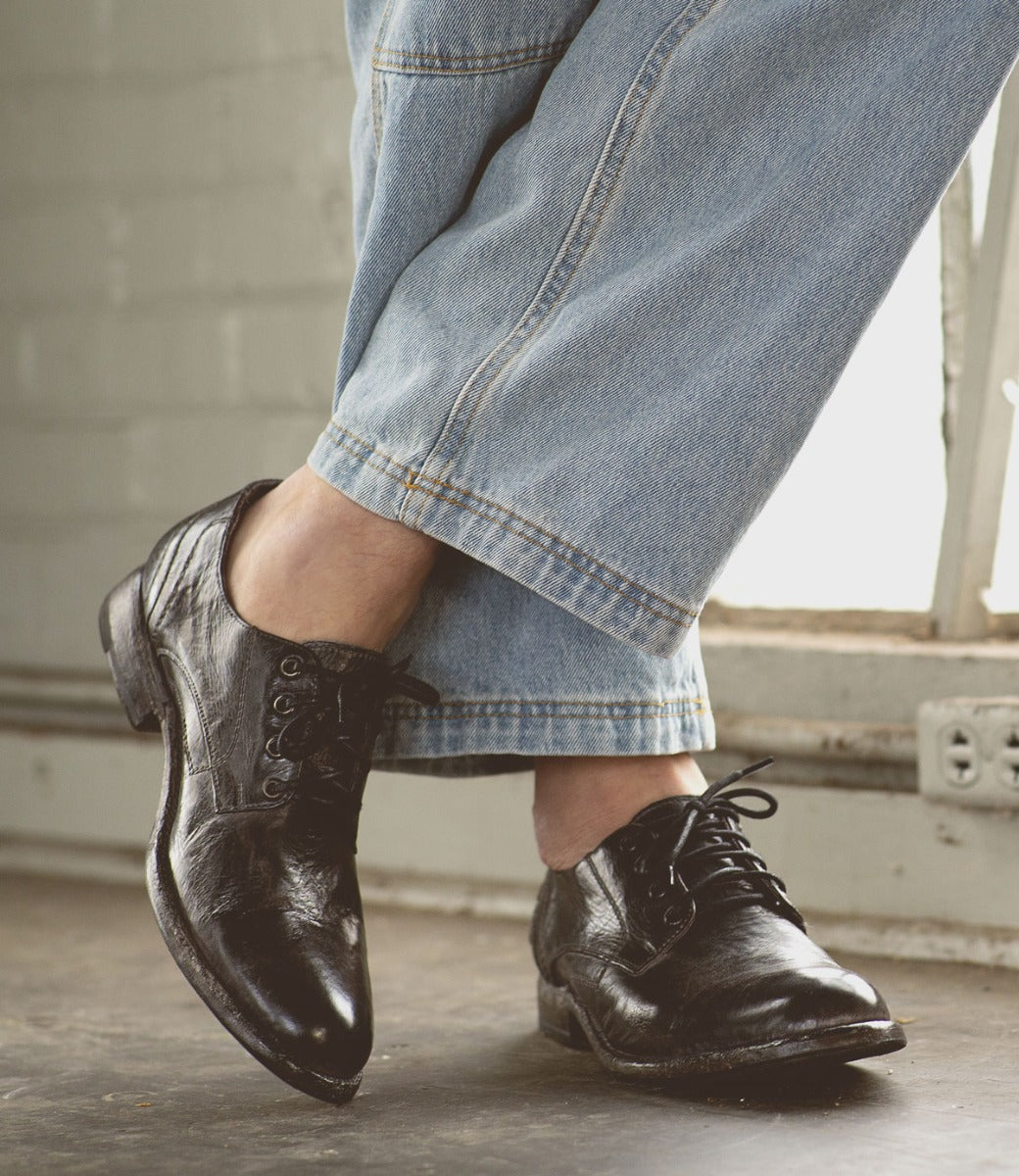 A person wearing jeans and a pair of Galao black oxford shoes by Bed Stu.